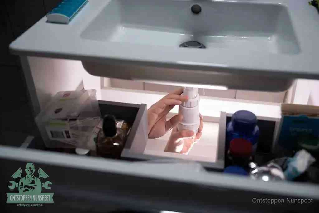 Een pompfles met zeep boven een wastafel, de heet water en afwasmiddel-methode om een vetprop in de afvoer los te maken in Nunspeet