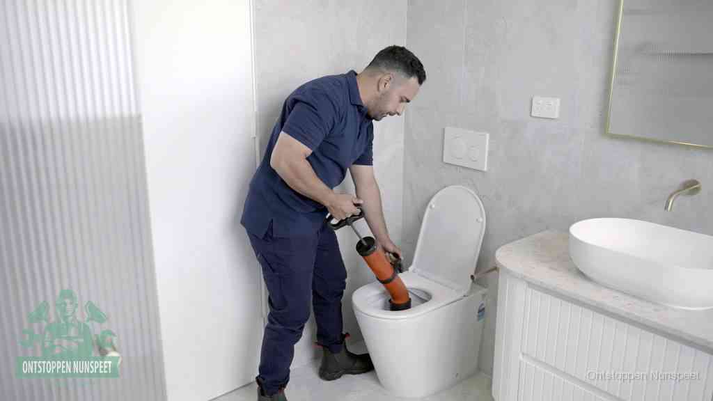 Een monteur buigt over een wandcloset en duwt met de hand een persluchtontstopper in de toiletpot om de verstopping handmatig los te maken in Nunspeet