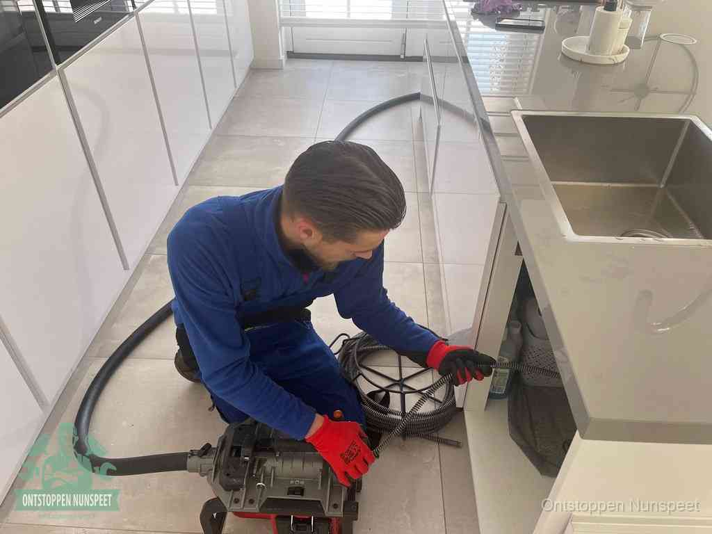 Een monteur ontstopt de keukenafvoer onder de spoelbak met een elektrische veermachine in Nunspeet