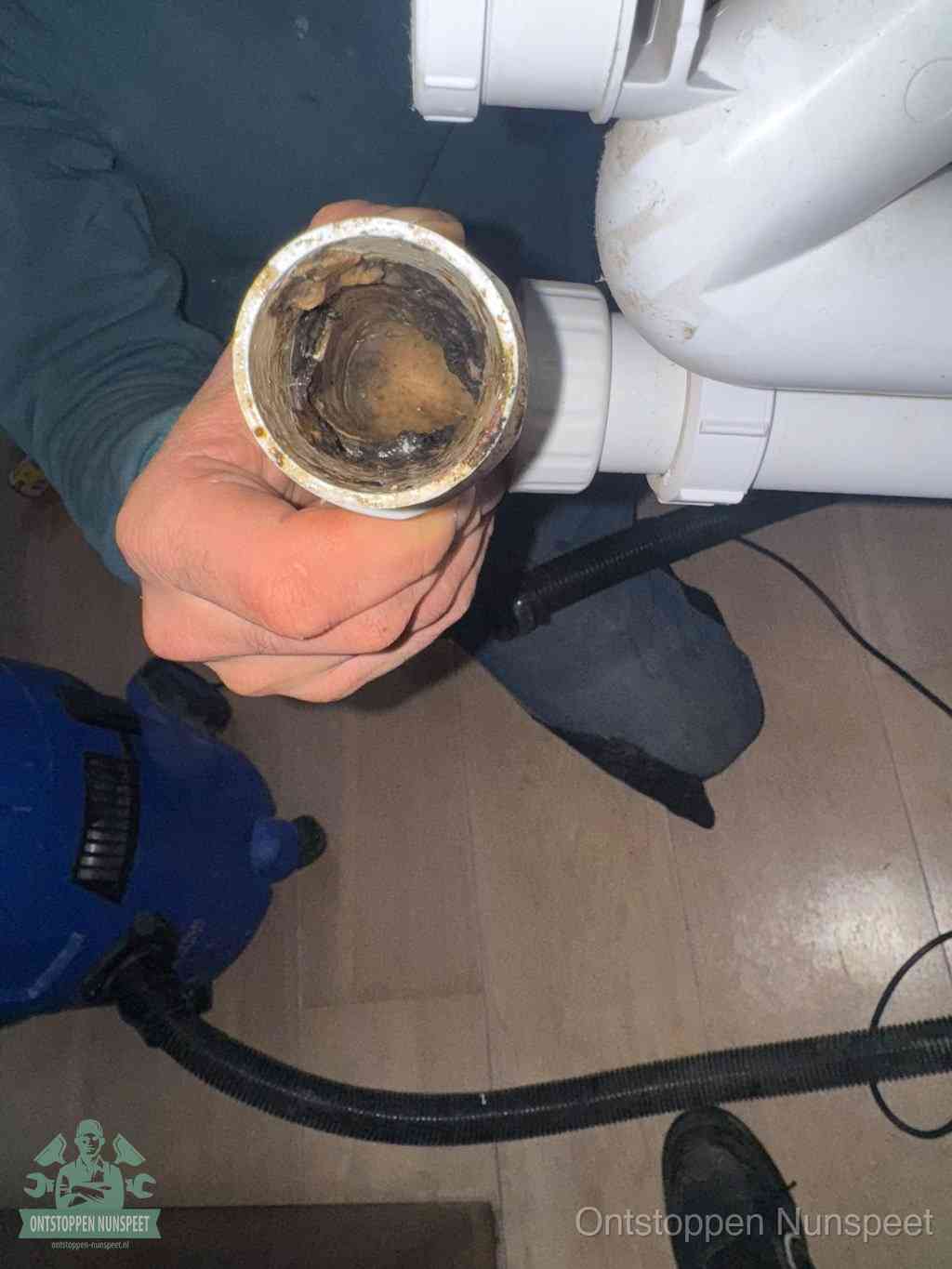 Een hand houdt een losgekoppeld PVC-afvoerbuisstuk vast dat van binnen volledig is dichtgeslibd met vet, vuil en aanslag, de meest voorkomende oorzaak van een verstopte afvoer in Nunspeet