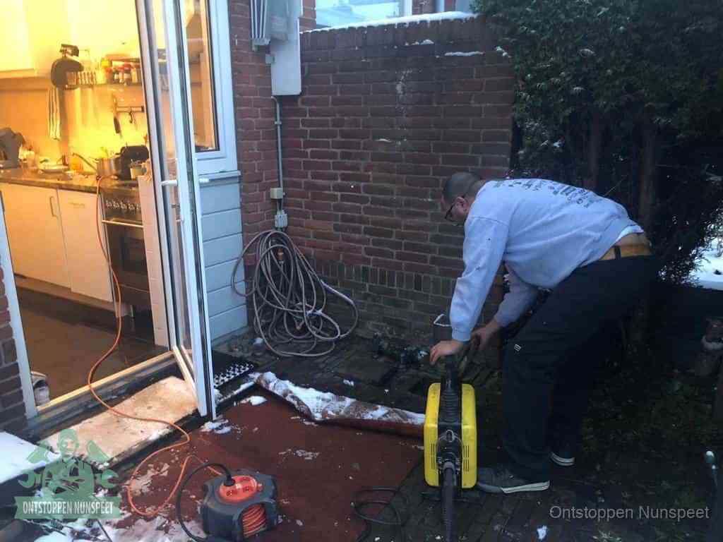 Een monteur werkt buiten bij een open riool-/grondput met een elektrische ontstoppingsmachine om een verborgen afvoerprobleem op te sporen in Nunspeet
