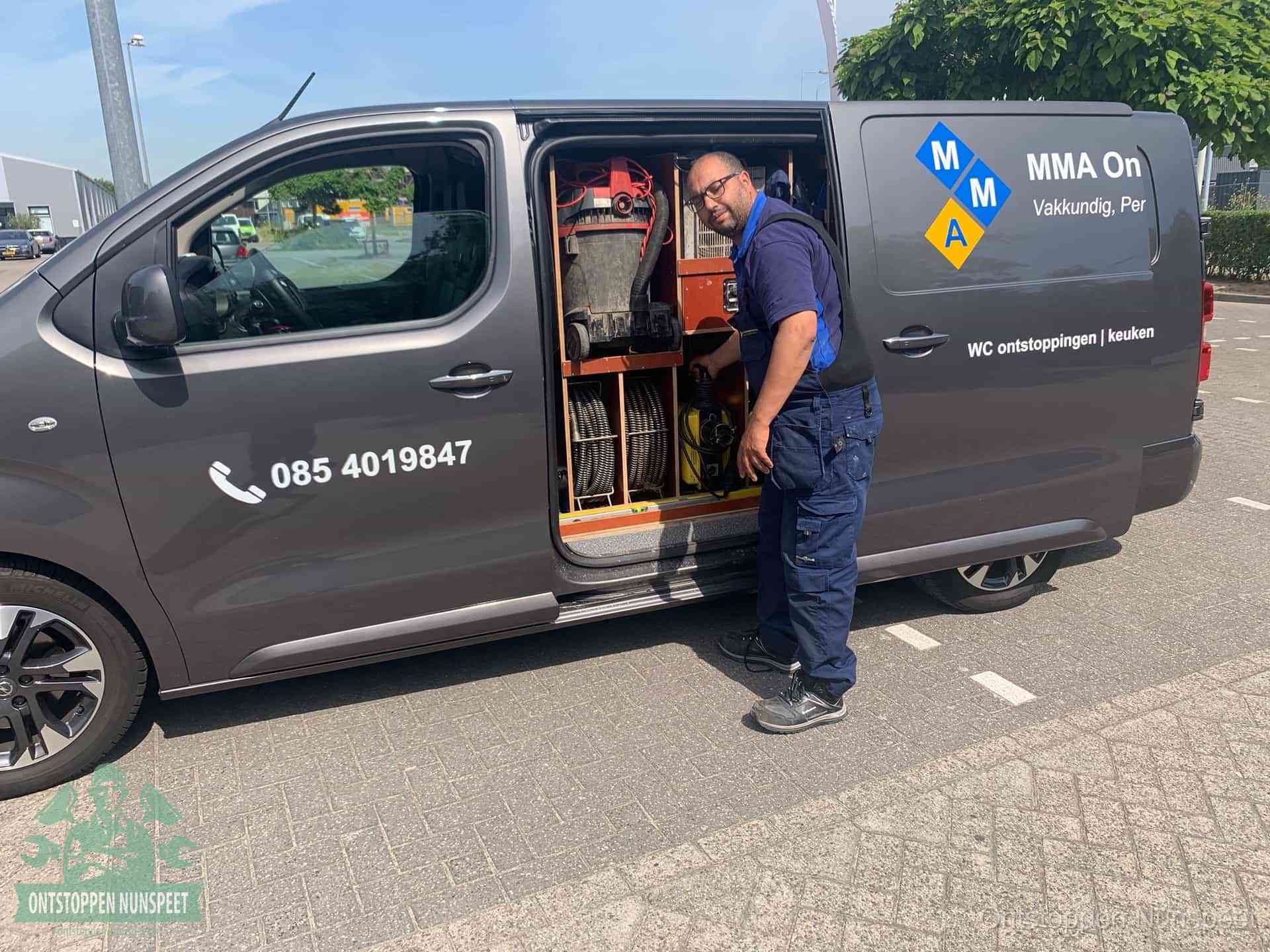 Een monteur bij de open schuifdeur van zijn bedrijfsbus op een parkeerplaats, klaar om de oorzaak van terugkerende afvoerverstoppingen aan te pakken in Nunspeet