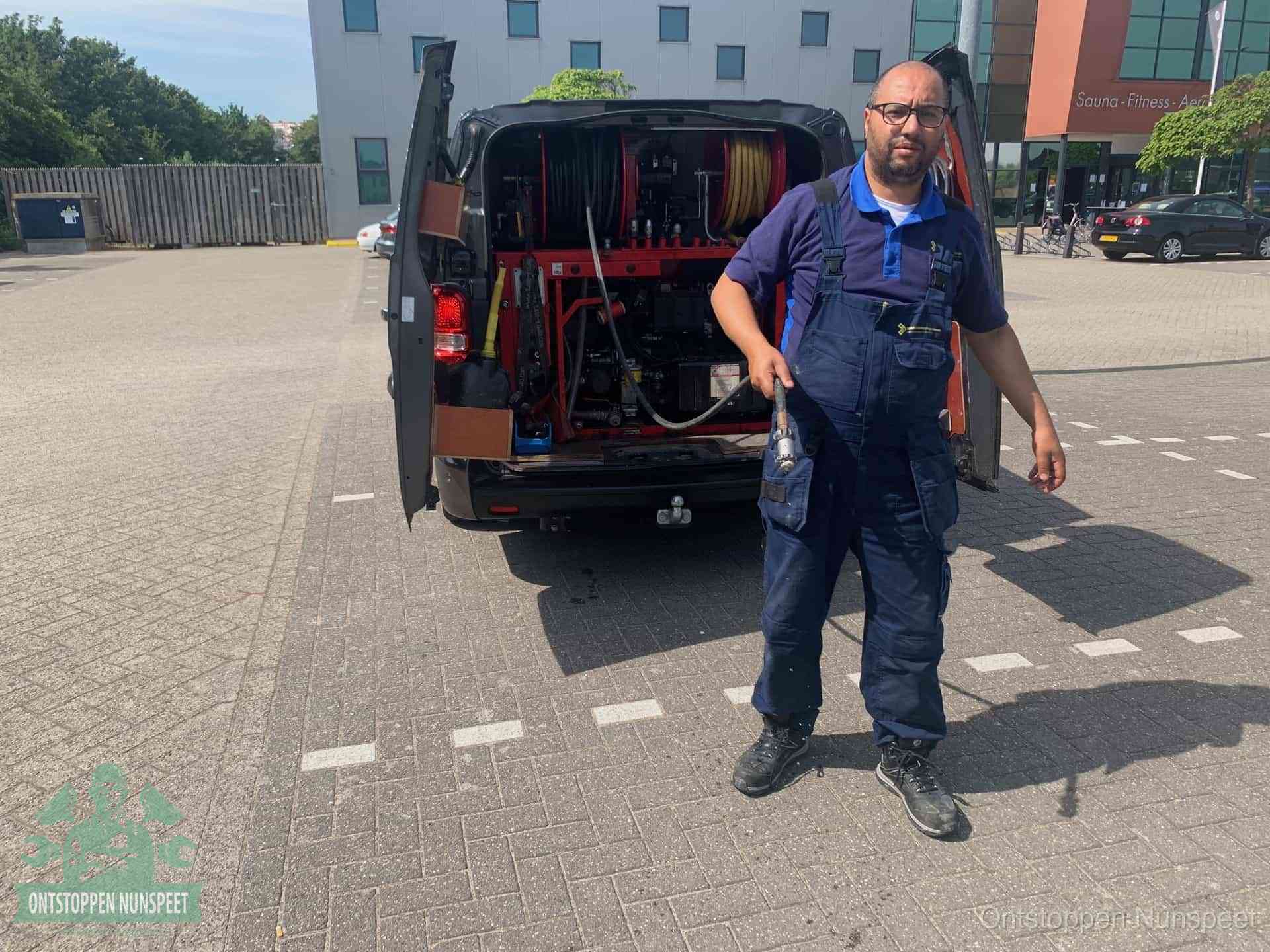 Een monteur bij zijn bestelbus met een hogedruk- en rioolreinigingsunit, klaar om de oorzaak van terugkerende wc-verstoppingen aan te pakken in Nunspeet