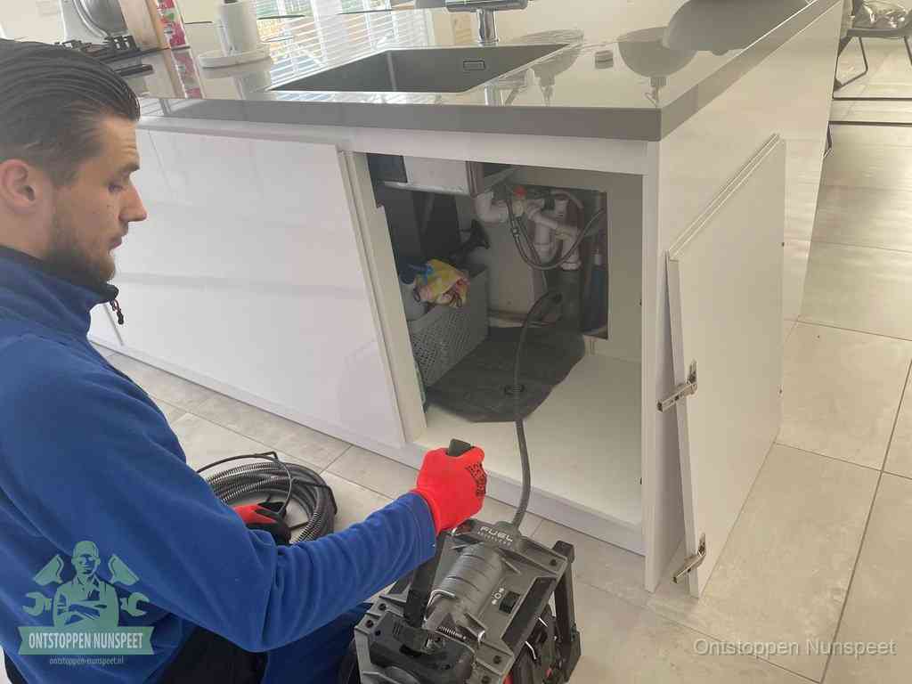 Monteur ontstopt met een veermachine een verstopte afvoer onder de gootsteen in Nunspeet