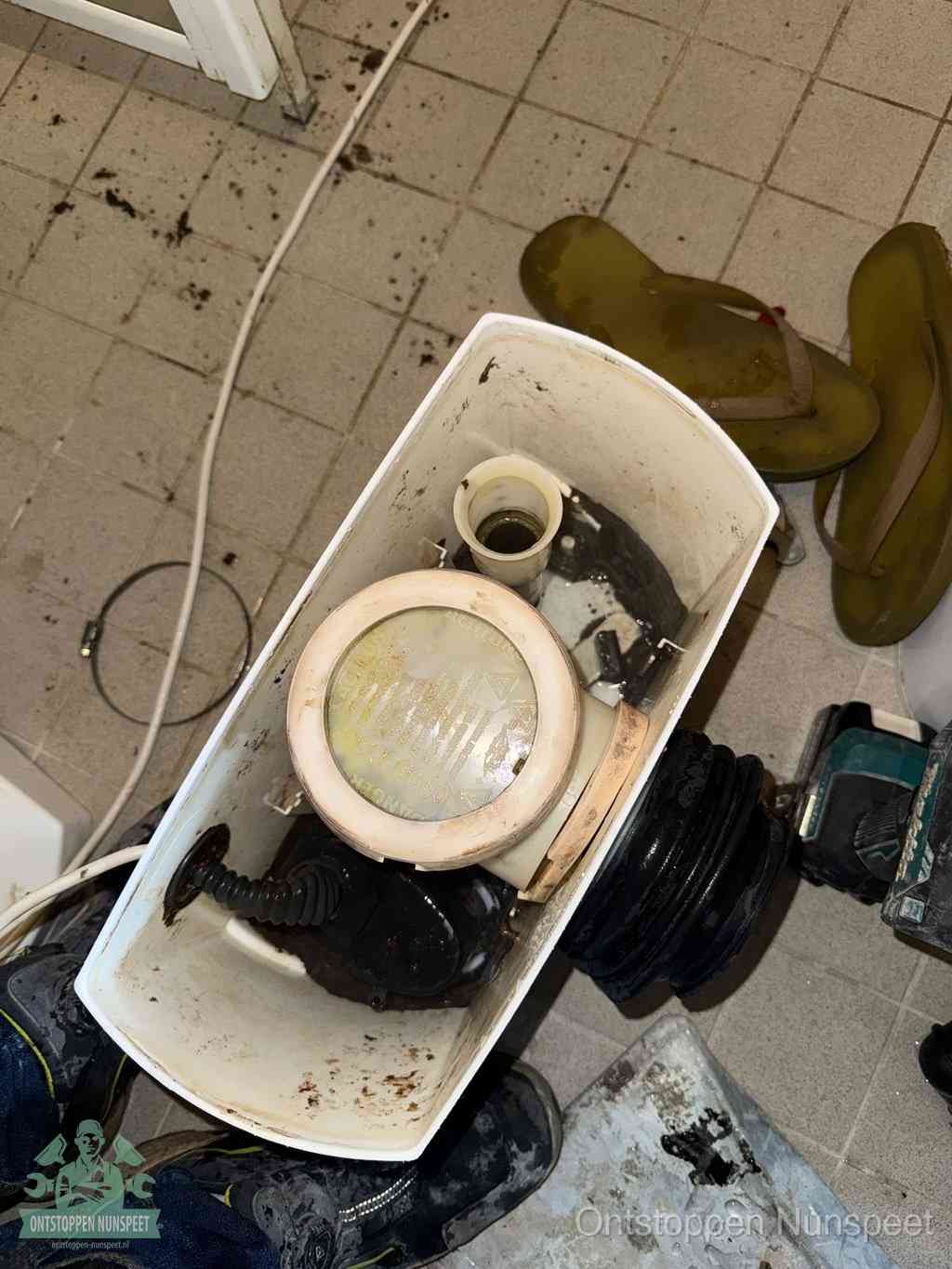 Een gedemonteerde toiletpot op de vloer met ontstoppingsveer en gereedschap ernaast, het verwijderen van een vastzittend voorwerp uit de wc in Nunspeet