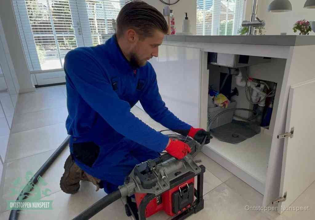 Een monteur voert een professionele elektrische ontstoppingsmachine in de afvoer onder de spoelbak tijdens het gootsteen ontstoppen in Nunspeet