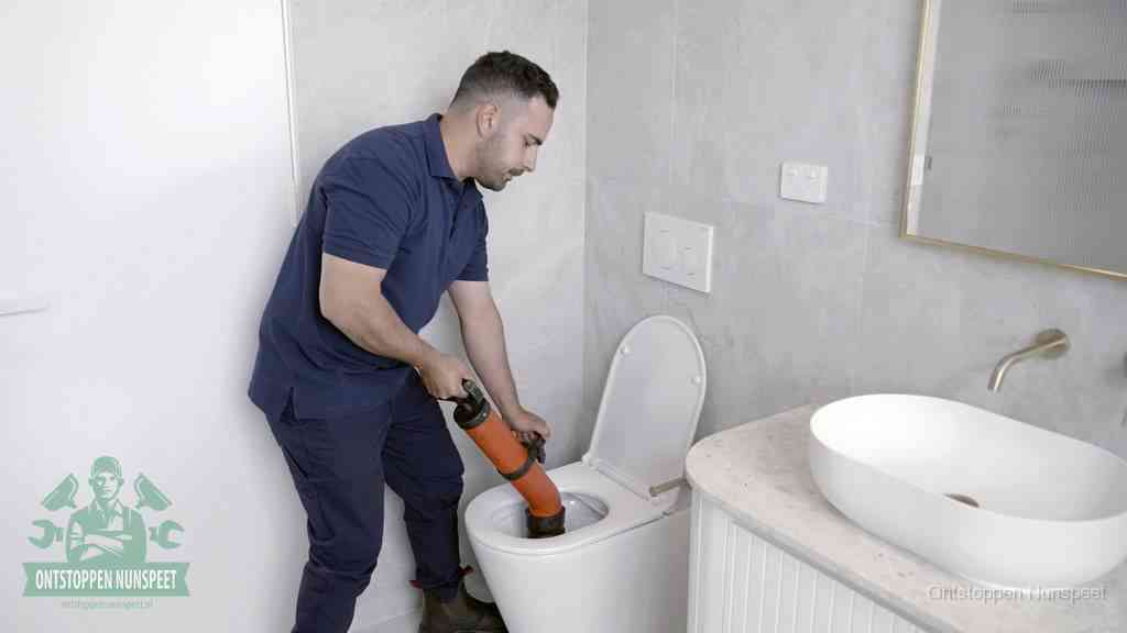 Een man gebruikt een handmatige luchtdruk-ontstopper in een modern betegeld toilet om zelf de wc te ontstoppen in Nunspeet